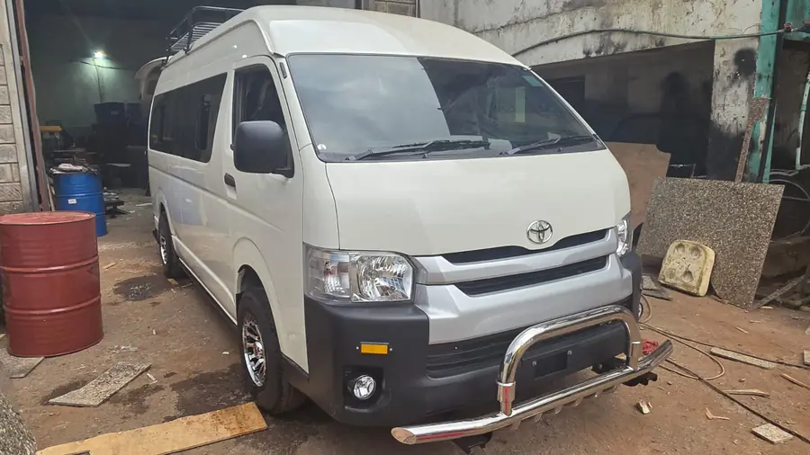 White high-roof Toyota Hiace with a chrome front bumper guard and roof rack
