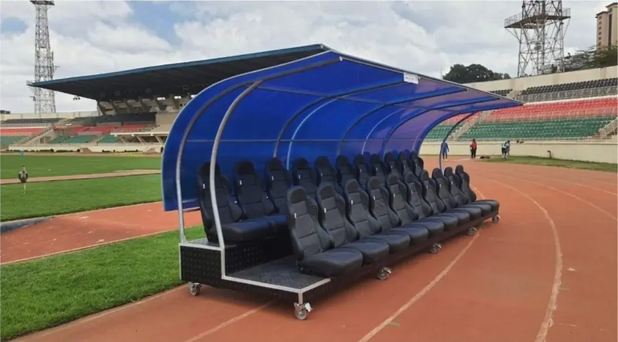 Blue-canopy team dugout with bucket seats beside a stadium track