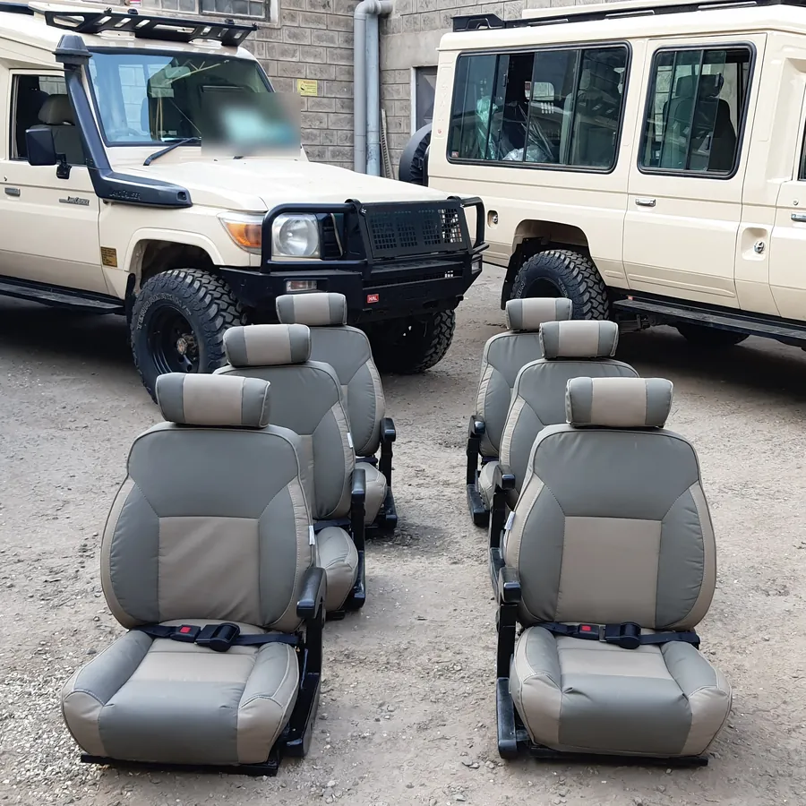 Two-tone seats lined up in the workshop yard beside two Land Cruisers, ready to fit
